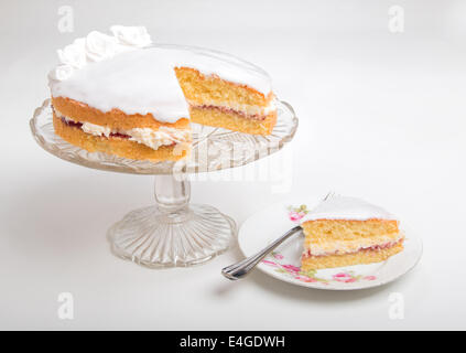 Gâteau éponge victoria iced in blanc avec des roses à la main sur socle en verre cake stand tranche de gâteau sur une plaque en dessous(42D 44 Banque D'Images