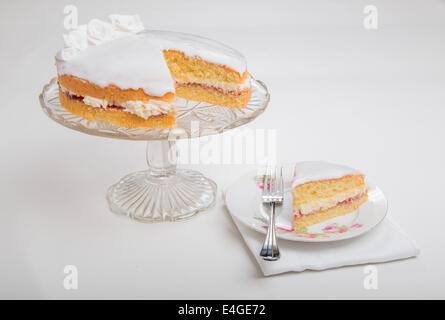 Gâteau éponge victoria iced in blanc avec des roses à la main sur socle en verre cake stand tranche de gâteau sur une plaque en dessous(41D 44 Banque D'Images