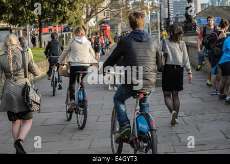 Les banlieusards ride Boris bikes parmi les piétons après le travail sur une promenade sur la rive sud de la Tamise, Londres, UK Banque D'Images