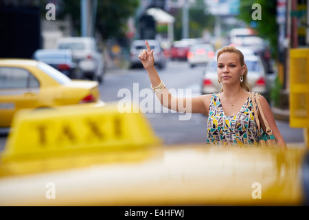 Blond businesswoman appelant taxi jaune avec bras levé en rue. Le tourisme et les voyages d'affaires Banque D'Images