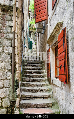 Vieux escaliers en pierre à travers une ruelle étroite aux volets rouges dans la vieille ville de Kotor, l'un des endroits les plus célèbres sur l'Adriatique Banque D'Images