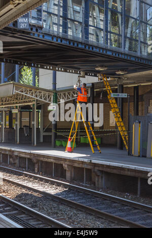 Cette image montre un ingénieur électrique travaillant sur le câblage sur la face inférieure d'une passerelle à une gare ferroviaire national Banque D'Images