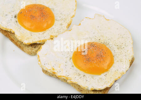 Deux oeufs au plat avec du sel et du poivre sur toast, Close up on white plate, full frame Banque D'Images