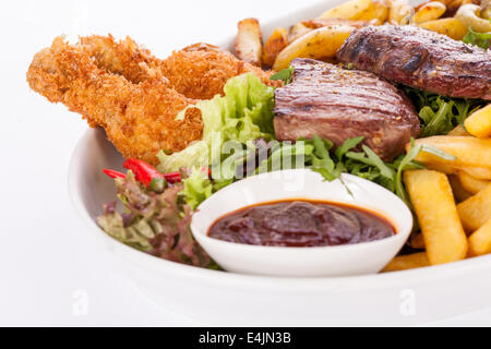 Petit plateau de viandes mixtes dont le steak grillé, crumbed croustillant de volaille et de bœuf sur un lit de légumes verts frais mélangé sa Banque D'Images