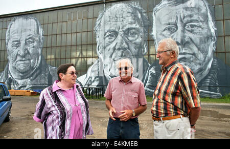 Monika anciens mineurs Mietsch (L-R), Hans-Georg Petschke et Horst Richter tenir devant dans le portraits grand format ouvert Ferropolis museum de Graefenhainichen, Allemagne, 09 juillet 2014. Le peintre Hendrik Beikirch crée 12 mètres de haut portraits de huit anciens mineurs de la mine à ciel ouvert Golpa-Nord sur le mur de l'ancien atelier de discussion ouverte. L'œuvre appelée 'Spuren' (lit : traces) a été présenté au public au cours de l''Splash' festival le 13 juillet 2014. Après la fin de l'extraction de lignite dans la "Ville du fer' (Ferropolis) en 1995, l'ancienne mine a été transformé en un musée en plein air exposant Banque D'Images