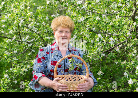 Femme mature avec panier d'osier dans le jardin au printemps Banque D'Images