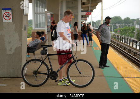 Merrick, New York, États-Unis - 14 juillet 2014 - Pendant l'heure de pointe du soir, un homme avec son vélo attend un train pour arriver sur une plate-forme surélevée de Merrick gare de Babylone, de la direction générale après MTA Metropolitan Transit Authority et Long Island Rail Road Union européenne parle de l'impasse, avec un potentiel d'LIRR imminente grève juste quelques jours auparavant. Credit : Ann E Parry/Alamy Live News Banque D'Images