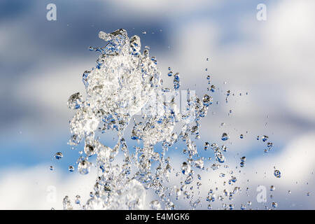 Gouttes de la fontaine de l'eau brillant pur contre nuages Banque D'Images