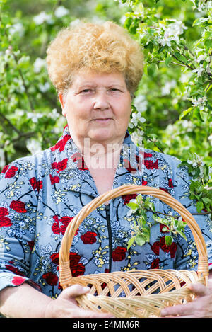 Femme mature avec panier d'osier dans le jardin au printemps Banque D'Images