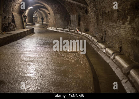 Petit homme à distance marche à travers un tunnel souterrain humide brillant Banque D'Images