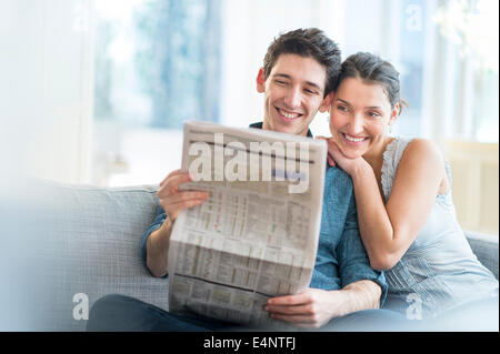 Couple reading newspaper on sofa Banque D'Images