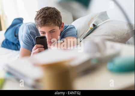 Teenage boy (16-17) lying on bed and text messaging Banque D'Images