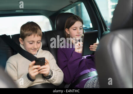 Boy and girl (8-9, 10-11) using digital tablet et smart phone in car Banque D'Images