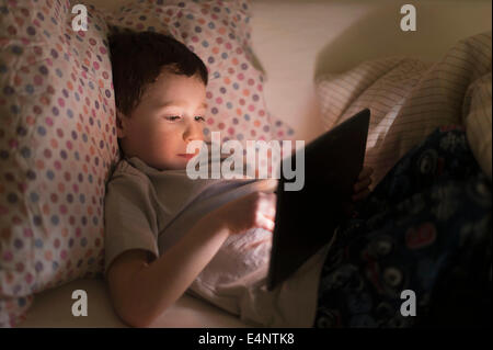 Boy (6-7) using digital tablet in bed Banque D'Images