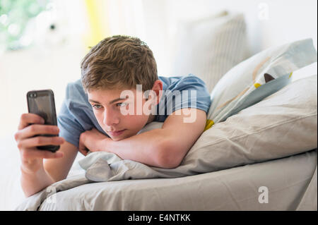 Teenage boy (16-17) lying on bed and text messaging Banque D'Images