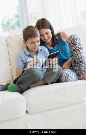 Boy and girl (8-9, 10-11) sitting on sofa using digital tablet Banque D'Images