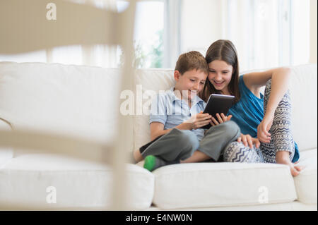 Boy and girl (8-9, 10-11) sitting on sofa using digital tablet Banque D'Images