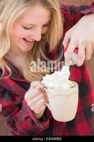 Portrait de femme de pulvériser la crème fouettée dans le chocolat chaud Banque D'Images