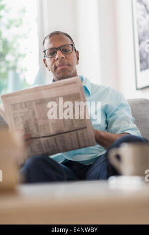 Man reading newspaper on sofa Banque D'Images