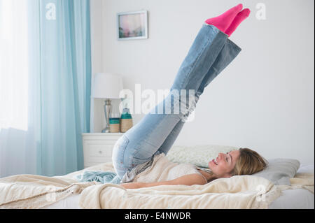 Young woman lying on bed with legs up Banque D'Images