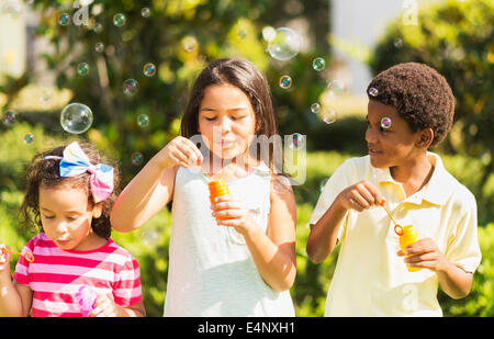 Les filles (4-5, 8-9) et garçon (6-7) blowing soap bubble Banque D'Images