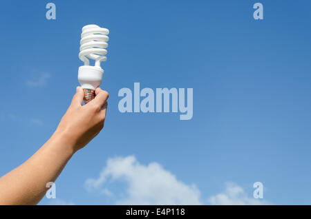 Main tenant ampoule à économie d'énergie sur fond de ciel bleu Banque D'Images