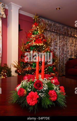 Décoration de table de Noël avec des roses rouges, les œillets et les bougies, l'arbre de Noël en arrière-plan Banque D'Images