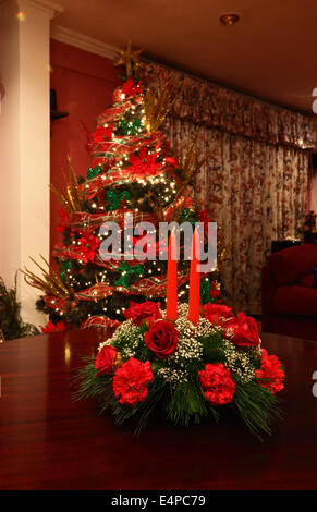 Décoration de table de Noël avec des roses rouges, les œillets et les bougies, l'arbre de Noël en arrière-plan Banque D'Images