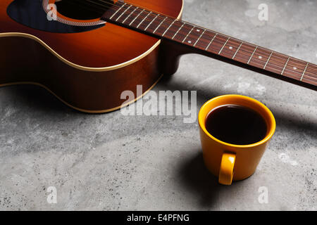 Une tasse de café chaud et une guitare sur une surface en béton. Banque D'Images