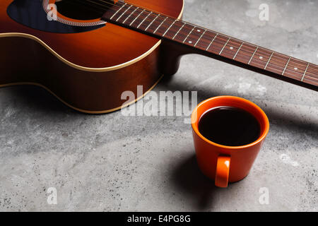 Une tasse de café chaud et une guitare sur une surface en béton. Banque D'Images