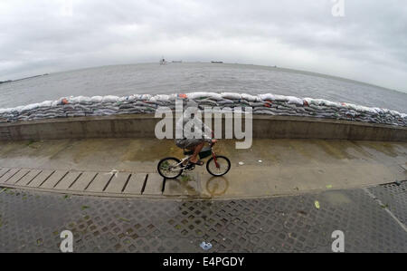 La province de Cavite, Philippines. 16 juillet, 2014. Un homme chevauche son vélo à côté de sacs de sable placés sur le baywalk pour éviter les dommages causés par le typhon Rammasun dans la province de Cavite, Philippines, le 16 juillet 2014. Au moins 5 personnes ont été tuées à la suite de l'assaut du typhon Rammasun (nom local : Glenda) qui a paralysé la capitale des Philippines, de Manille, mercredi. Credit : Rouelle Umali/Xinhua/Alamy Live News Banque D'Images