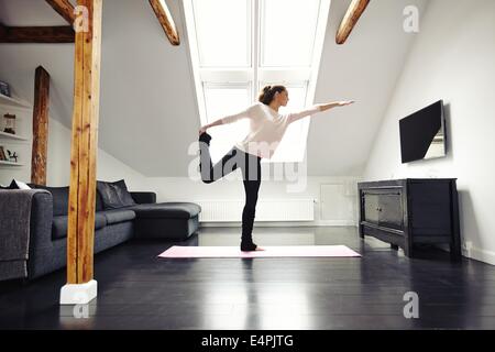 Femme de remise en forme de l'exercice dans la salle de séjour. L'étirement et en équilibre sur une jambe à la maison. Portrait femme pratiquant le yoga. Banque D'Images