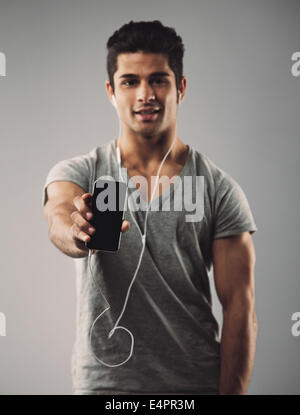 Young man wearing earphones montrant son nouveau téléphone mobile. Modèle masculin hispaniques afficher son smart phone Banque D'Images