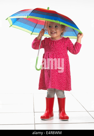 Petite fille (2 ans) portant des bottes wellington et holding umbrella Banque D'Images