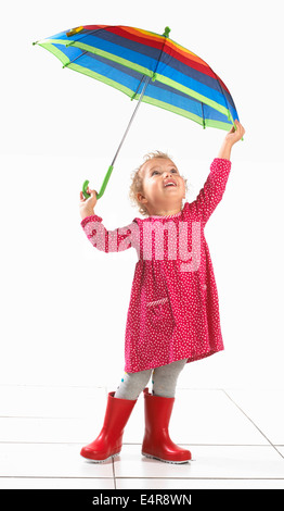 Petite fille (2 ans) portant des bottes wellington et holding umbrella Banque D'Images