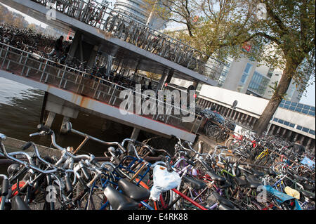 Les vélos garés dans un parc de plusieurs étages et par le côté du canal à Amsterdam, Pays-Bas. Banque D'Images