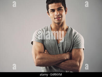 Portrait of muscular young man standing avec les bras croisés contre l'arrière-plan gris. Macho man en toute confiance. Banque D'Images