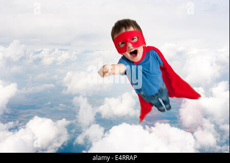 Super héros garçon enfant battant vers le haut dans le ciel à travers les nuages Banque D'Images