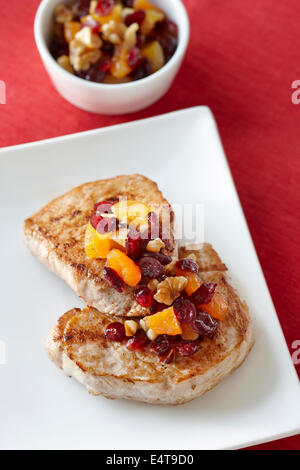 Porkchops sur platine habillé avec les canneberges, les noix, et les abricots séchés, bol de vinaigrette supplémentaire à l'arrière-plan Banque D'Images