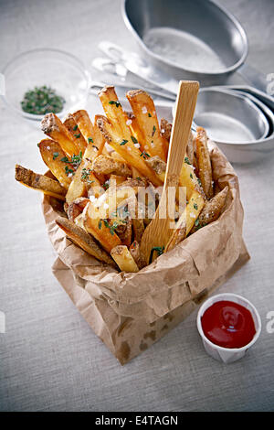 Frites assaisonnées en sac de papier avec du ketchup et de la fourche, Studio Shot Banque D'Images