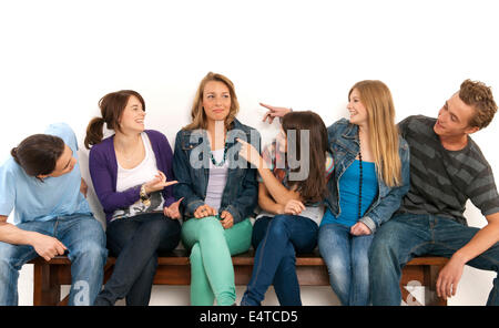 Six jeunes hommes et femmes, assis sur un banc ensemble, de rire et de se regarder, studio shot on white background Banque D'Images