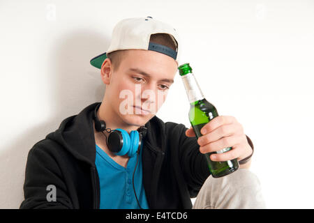 Teenage boy wearing hat avec des écouteurs autour du cou, tenant une bouteille de bière, studio shot on white background Banque D'Images