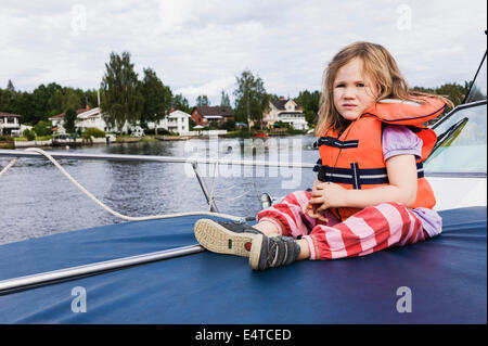 3 ans, fille en gilet orange assis sur le dessus du bateau, amarré sur le lac, la Suède Banque D'Images