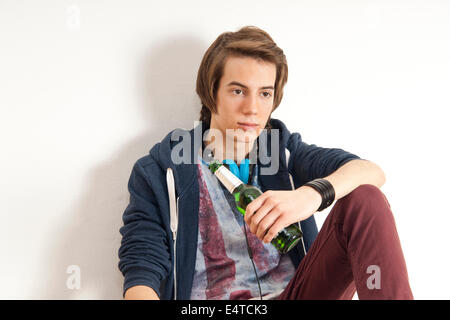 Teenage boy portant des écouteurs autour du cou et tenant une bouteille de bière, studio shot on white background Banque D'Images