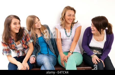 Quatre jeunes femmes, assis sur un banc ensemble, de rire et de se regarder, studio shot on white background Banque D'Images