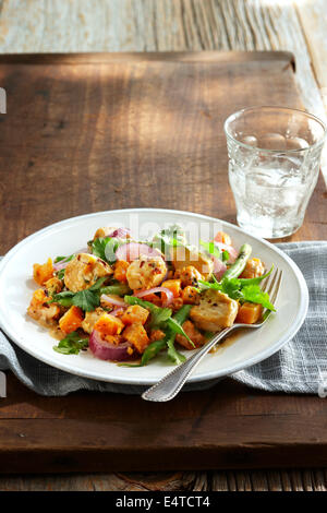 Sauté de poulet aux arachides avec oignons rouges, haricots verts, carottes, coriandre et piments sur plaque avec fourchette et un verre d'eau Banque D'Images