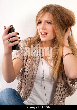 Jeune, blond, long-haired woman staring at cellphone avec incrédulité, studio shot on white background Banque D'Images