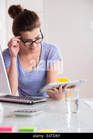 Jeune femme à l'aide d'ordinateur portable et tablette ordinateur, travaillant en bureau, studio shot Banque D'Images