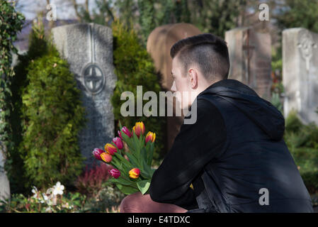 Adolescent accroupi en face de pierres tombales du cimetière de Banque D'Images