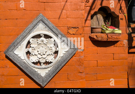 Jimbaran, Bali, Indonésie. L'épargne (Canang) dans un renfoncement du mur à côté d'entrée d'un restaurant. Décoration fleur de lotus. Banque D'Images